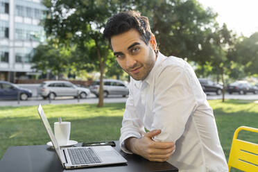 Confident businessman with laptop on table sitting at sidewalk cafe - AFVF07135
