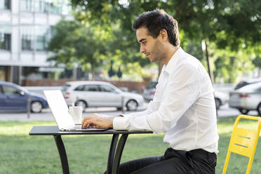 Männlicher Unternehmer arbeitet an einem Laptop auf einem Tisch in einem Straßencafé - AFVF07139