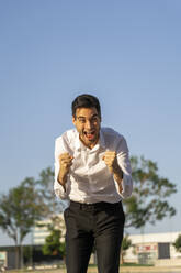 Successful businessman screaming while gesturing against clear blue sky - AFVF07164