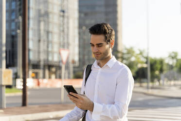 Businessman using smart phone while standing on street in city - AFVF07168