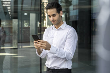 Männlicher Berufstätiger, der ein Smartphone benutzt, während er im Büro am Fenster steht - AFVF07189