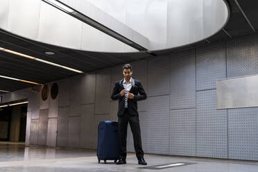Geschäftsmann mit Gepäck auf Rädern steht auf dem Boden am Bahnhof - AFVF07212