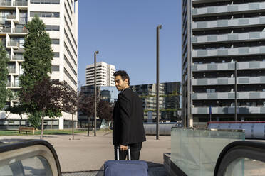 Geschäftsmann mit Koffer zu Fuß auf dem Gehweg gegen den klaren Himmel in der Stadt - AFVF07216