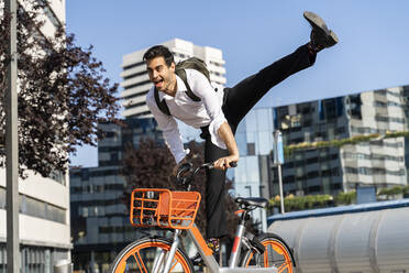 Fröhlicher Geschäftsmann bei einem Stunt auf einem Elektrofahrrad in der Stadt - AFVF07218