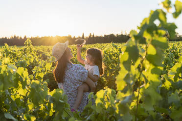 Mutter hält ihre Tochter in einem Weinberg bei Sonnenuntergang in der Provence, Frankreich - GEMF04116