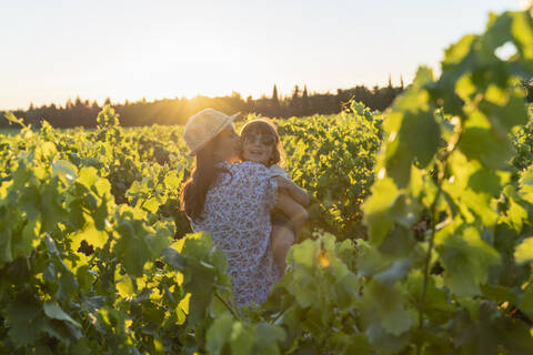 Mother holding her daughter in a vineyard at sunset in Provence, France stock photo