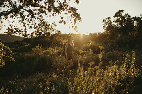 Frau schaut weg, während sie bei Sonnenuntergang im Wald steht - DMGF00133
