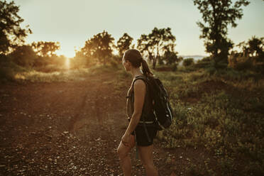 Female trekker looking at sunset view while standing in forest - DMGF00137