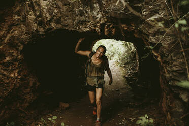 Weiblicher Wanderer in Höhle im Wald stehend - DMGF00142