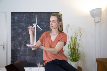 Frau im Büro hält Modell einer Windkraftanlage - FKF03816