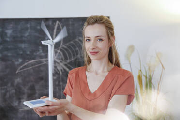 Portrait of confident woman in office holding wind turbine model - FKF03817