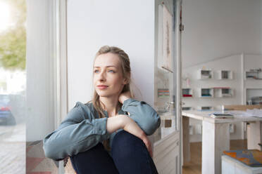 Relaxed woman having a break in home office looking out of window - FKF03828