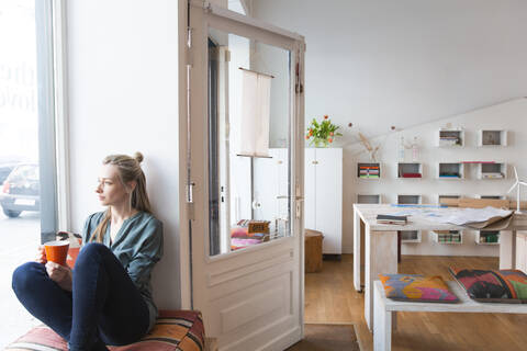 Entspannte Frau, die eine Pause im Büro zu Hause macht und aus dem Fenster schaut, lizenzfreies Stockfoto