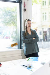 Portrait of woman leaning against glass door in office - FKF03837