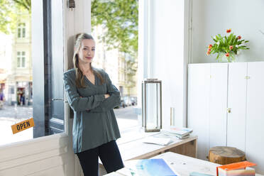 Portrait of woman leaning against glass door in office - FKF03838