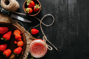 Top view of tasty homemade strawberry juice in glass jar placed near bowl with ripe berries on black wooden background - ADSF14197