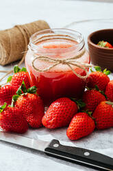 Composition with fresh homemade strawberry juice in glass jar wrapped with twine placed on marble surface with whole berries and knife - ADSF14199