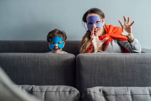 Fröhliche Frau und kleiner Junge mit Papiermasken spielen am Wochenende und tun so, als wären sie Superhelden, während sie in die Kamera schauen - ADSF14200