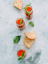 From above of glass bottles with fresh cold gazpacho soup on rough gray surface with toasts and basil - ADSF14221