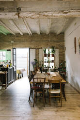 Großer Holztisch und Stühle in rustikaler Bar im Retrostil mit schäbiger Decke und grünen Topfpflanzen am Fenster - ADSF14228