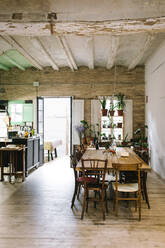 Large wooden table and chairs in rustic retro styled bar with shabby ceiling and potted green plants on window - ADSF14229