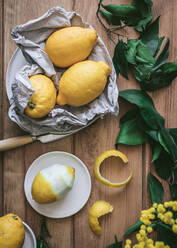 Draufsicht auf geschälte und frische Zitronen auf Tellern auf Holztisch mit grünen Blättern und gelben Blumen - ADSF14234