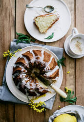Draufsicht von oben leckerer frischer veganer Kuchen mit Zitrone und Kokosnuss mit Glasur auf Holztisch mit Zutaten - ADSF14238