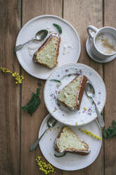 Draufsicht auf Scheiben von frischem veganem Zitronen-Kokos-Kuchen auf Tellern mit Löffeln und einer Tasse Kaffee - ADSF14239