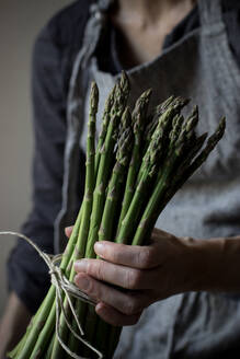 Crop woman in gray textured dress holding tenderly heap of fresh green asparagus stems - ADSF14247