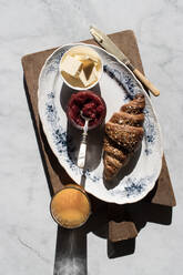 Draufsicht auf einen Teller mit knusprigem Croissant und Butter und Erdbeermarmelade, serviert auf einem Tisch mit einem Glas Orangensaft - ADSF14291