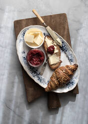 Draufsicht auf einen Teller mit knusprigem Croissant und Butter und Erdbeermarmelade auf einem Holzbrett - ADSF14292