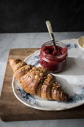 Draufsicht auf einen Teller mit knusprigem Croissant und Erdbeermarmelade auf einem Holzbrett - ADSF14293