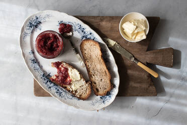 Draufsicht auf einen Teller mit knusprigem Croissant und Butter und Erdbeermarmelade auf einem Holzbrett - ADSF14294