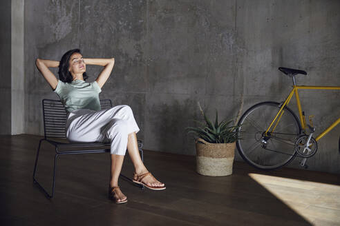 Weibliche Unternehmerin mit geschlossenen Augen, die sich auf einem Stuhl an der Wand im Büro ausruht - MCF01208