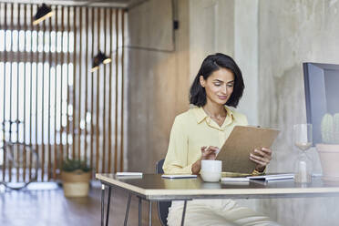 Businesswoman holding clipboard while working at desk in office - MCF01231