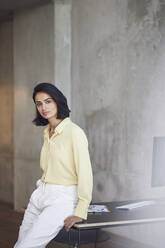 Serious female entrepreneur sitting on desk against wall in office - MCF01239