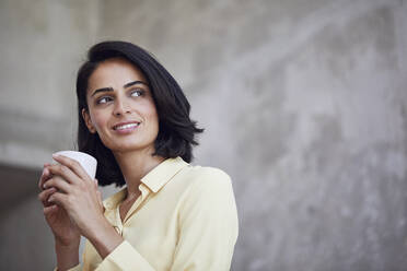 Close-up of thoughtful businesswoman holding coffee cup against wall in office - MCF01243