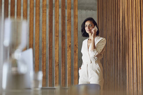 Female entrepreneur talking over mobile phone while standing at entrance in office - MCF01254