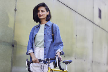 Nachdenkliche Pendlerin mit Fahrrad an einer Mauer in der Stadt stehend - MCF01269