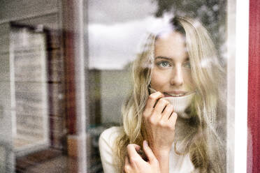 Nahaufnahme einer Geschäftsfrau mit Rollkragenpullover, die durch das Fenster eines Büros schaut, gesehen durch Glas - PESF02070