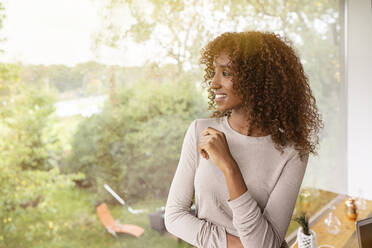 Thoughtful businesswoman with curly hair looking through window in office - PESF02073