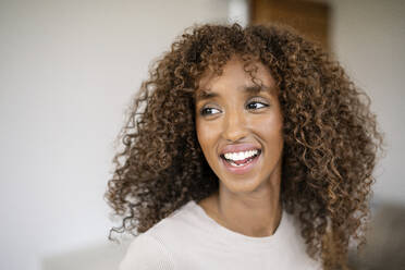 Close-up of cheerful businesswoman with curly hair looking away against wall in office - PESF02078