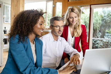 Male manager discussing over laptop with female colleagues in office - PESF02091