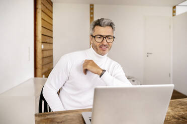 Lächelnder reifer männlicher Unternehmer mit Laptop auf dem Schreibtisch im Büro - PESF02113