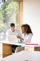 Smiling male and female coworker planning over laptop on desk in office - PESF02129