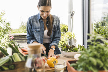 Smiling young woman chopping vegetables on cutting board in yard - UUF21000