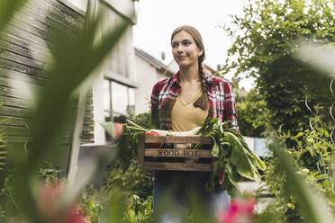 Young woman carrying crate looking away while standing in vegetable garden - UUF21008