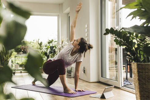 Young woman with digital tablet exercising on mat at home - UUF21032