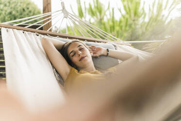 Young woman with arms raised sleeping on hammock in yard - UUF21050