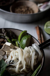 From above of arranged bowls with dry spices and served Pho soup with noodles on marble board - ADSF14331